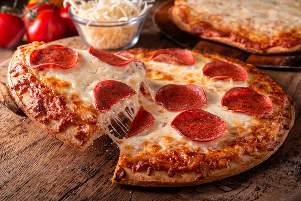 Pepperoni and four cheese pizzas on a rustic wood table top.